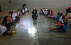 Crianças sentadas em meio circulo e fazendo alongamentos.