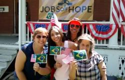 Professoras da rede municipal de ensino participam de celebração do 4 de julho nos Estados Unidos. Na foto, 4 mulheres seguram bandeirinhas do Brasil e dos Estados Unidos