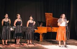 No palco, atrizes encenam o musical "As Rainhas do Rádio": uma está cantando à frente de um piano de cauda e, ao lado dela, três mulheres fazem "baking vocal".