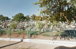 Grade e túmulos do Cemitério da Saudade durante o dia, com copa de árvore à direita.