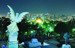 Cemitério do Bonfim à noite com Anjo de sepultura de constas em primeiro plano. Ao fundo, cidade iluminada. 