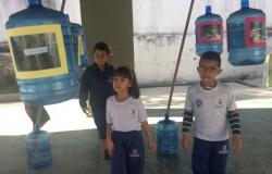 Três crianças da Rede Municipal de Ensino percorrem ambiente com fotos de imagens ecoeducativas coladas à galões d'água