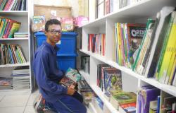 Aluno de escola municipal, ajoelhado, escolhendo livros em uma prateleira.