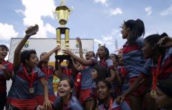 Cerca de doze integrantes da equipe feminina de futebol Tupinambás, campeâ de 2016, erguem a taça e comemoram.