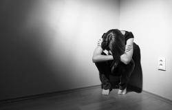 Imagem em preto e branco de pessoa encolhida em um canto, representando um paciente com sofrimento mental