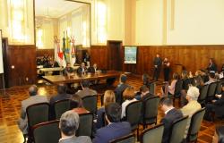 Posse do Novo Conselho Municipal de Turismo no Salão Nobre da Prefeitura de Belo Horizonte: ao fundo, mesa oficial com prefeito e duas autoridades, à frente, membros do conselho e convidados de costas, sentados. 