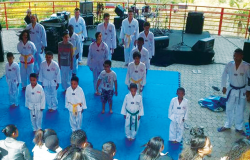 Cerca de quinze crianças praticam Tae-Kwon-Do em local coberto.
