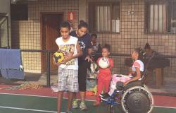 Quatro crianças reunidas para a prática esportiva: uma delas é cadeirante e outras duas estão com bola nas mãos.