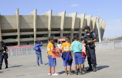 Cerca de quatro crianças são auxiliadas por guarda municipal sobre como soltar pipa de maneira segura na área externa do Mineirão.