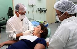 Dentista atende paciente acompanhado de auxiliar. Foto ilustrativa.