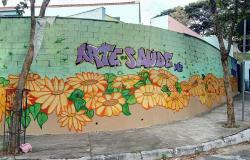 Muro de uma esquina pintado de verde com flores de pétalas amarelas e os dizeres "Arte da Saúde" em roxo.