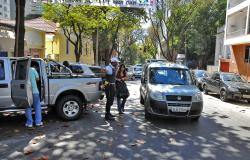 Carros estacionados, pedestres circulando e Guarda Municipal orientando o trânsito