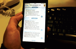 Mão de homem segura celular com aplicativo Telegram da Defesa Civil.