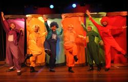 Seis atores, cada um vestido de uma das cores: roxo, amarelo, azul, verde, laranja e vermelho, dançam à frente de fundo colorido. 