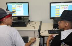 Dois estudantes, cada sentdo um em frente a um computador, se olham. Nas telas, a página do Orçamento Participativo da Criança e do Adolescente (OPCA). 