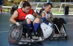 Dois jogadores de rugby em cadeiras de rodas em ação em quadra de esportes. 