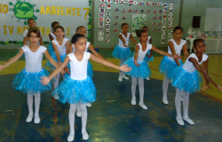Dez alunas com roupas de balé apresentam coreografia na quadra da escola.