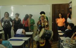 Mulher instrui alunos sobre coleta seletiva em escola municipal.