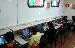 Cinco crianças em frente a laptops dentro da Carreta do Conhecimento. 