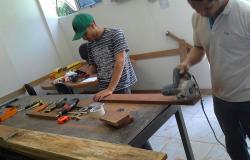 Um homem e um jovem de boné constróem carrinho de rolimã em oficina. 