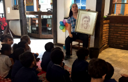 Crianças observam mulher sentada com desenho de outra mulher na mão