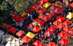 Vista aérea da Feira de Artes e Artesanato da Avenida Afonso pena, com cobertura das barraquinhas vermelhas em destaque e pessoas circulando entre elas. 