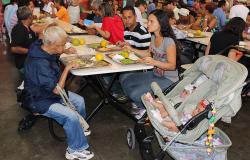 Cidadãos almoçam em restaurante popular, à direita, ao lado de uma mulher, um carrinho dois bebês. 