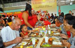 Cidadãos almoçam no restaurante popular enquanto pessoas vestidas de papai noel distribuem presentes