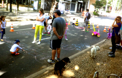 Crianças brincam de jogo da amarelinha e outras atividades em rua interditada da Savassi, acompanhadas por adultos.
