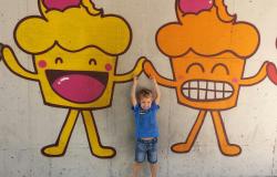 Criança 'dá as mãos' a dois bolinhos sorridentes pintados na parede.
