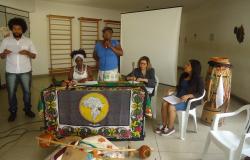 Cinco pessoas, com mesa com tambores e adereços afro, participam de Roda de Conversa sobre igualdade racial no Cras Lagoa.