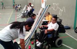 Criança com mobilidade reduzida em cadeira de rodas tem equipamento para jogar bocha colocado por técnica da Secretaria Municipal de Esportes.