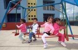 Quatro crianças de até 3 anos brincam em brinquedo de playground. 
