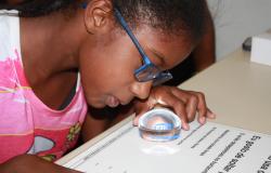 Menina com baixa visão usa óculos e lupa para ler