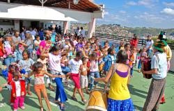 Cerca de 50 crianças participam de momento lúdico em escola durante as férias. Músicos se apresentam com tambores e fantasias.