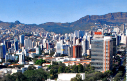 Cidade de Belo Horizonte, com muitos prédios e céu azul, durante o dia. Ao fundo, Serra do Curral.