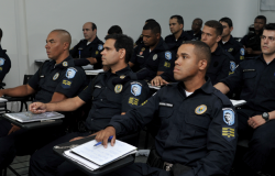 Mais de doze guardas municipais sentados em carteiras, fazendo curso de capacitação.