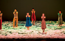 Seis atores fazem apresentação em palco com chão rosa e verde. 
