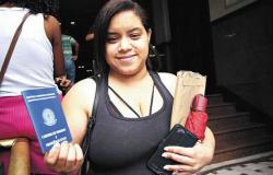 Uma jovem com a carteira de trabalho em mãos em frente ao SINE