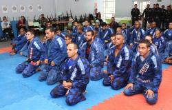 Vinte e um guardas municipais de uniforme azul, ajoelhados, em cerimônia de troca de faixa de Jiu-Jitsu