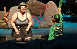 Atriz com roupa estilizada de balho conversa com homem fantasiado de jacaré, vestido de verde com escamas em cenário teatral aquático.
