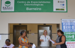 Atendente do Centro de Especialidades Odontológicas Barreiro Atende a duas mulheres de pé, à esquerda, uma outra mulher está sentada. 