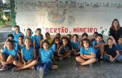 Dezesseis alunos sentados no chão da Escola Municipal Minervina Augusta, acompanhados de professora. Ao fundo um cartaz com os dizeres: "Sertão Mineiro".