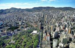 Vista aérea de BH, no centro, a avenida Afonso Pena, à esquerda, à frente, o Parque Municipal e ao fundo, a Serra do Curral e o céu. 