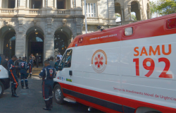 Cinco funcionários do SAMU ao lado de ambulância. 