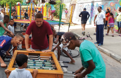 Cinco garotos brincam de pebolim (totó); ao fundo, crianças brincam no BH é da Gente da avenida Silva Lobo. 