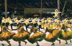 Mais de vinte membros de quadrilha junina fazem apresentação, vestidos de roupas juninas nas cores verde e amarelo. 