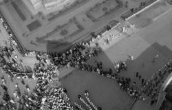 Foto histórica aérea em preto e branco de parte da cidade de Belo Horizonte, com mais de cinquenta pessoas, no tamanho de pontos pequeninos, a transitar pela rua. 