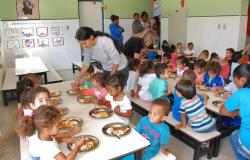 Mais de vinte crianças de 3 anos de idade almoçam, sob a supervisão de profissional da Secretaria Municipal de Educação. 