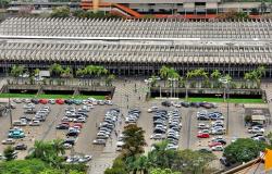 Imagem aérea do erminal Rodoviário Governador Israel Pinheiro (TERGIP), com prédio retambular e estacionamento com mais de trinta carros á frente, durante o dia. 